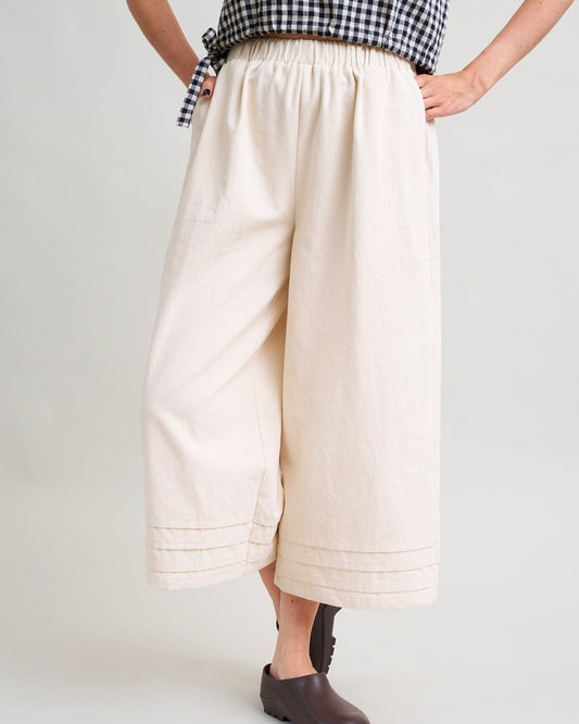 Person wearing a checkered top and beige wide-leg pants on a white background