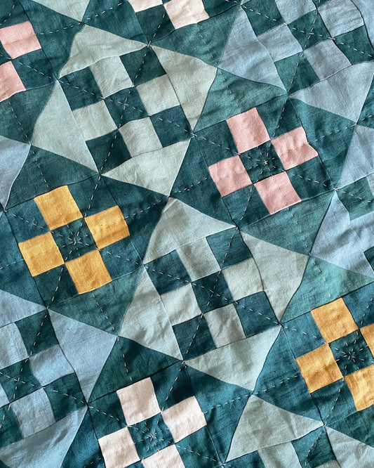 Close-up of a quilt with a Nine Patch Quilt design featuring geometric patterns in blue, pink, and yellow.